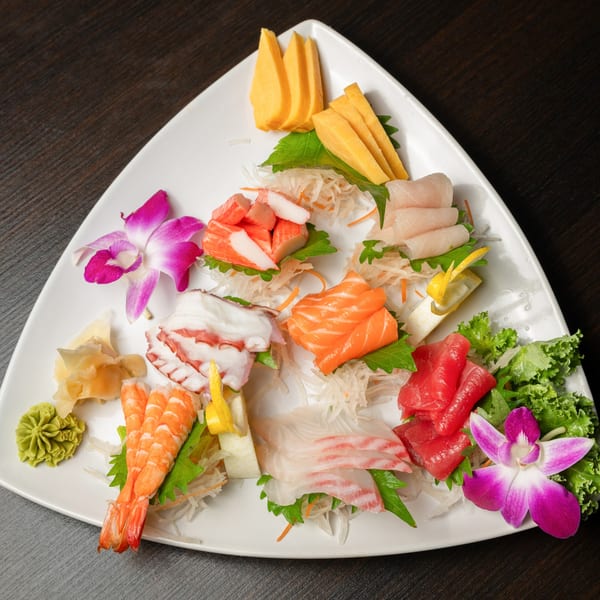 A triangular white plate filled with various sashimi, including salmon, tuna, shrimp, and octopus, garnished with orchids.