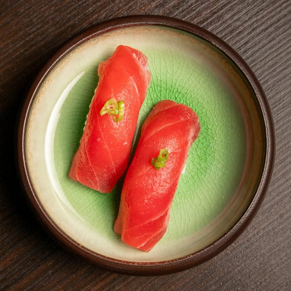 Two pieces of vibrant red tuna nigiri sushi, garnished with green onions, on a crackled green plate.