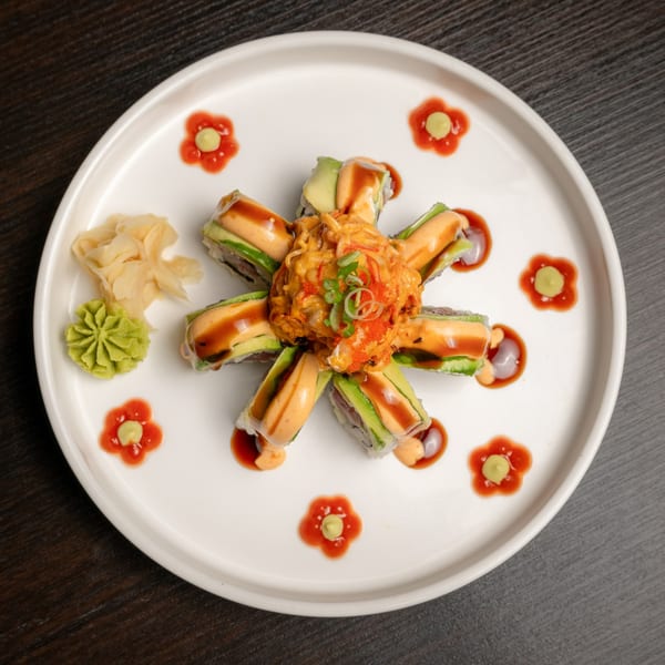 Sushi Alive's sushi roll with avocado, spicy crab, and sauces, garnished with ginger and wasabi.