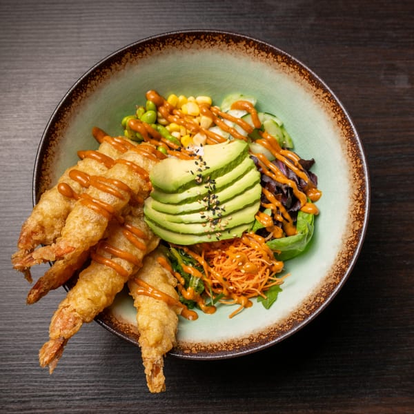 Tempura shrimp with avocado, corn, edamame, and greens, drizzled with orange sauce in a bowl.