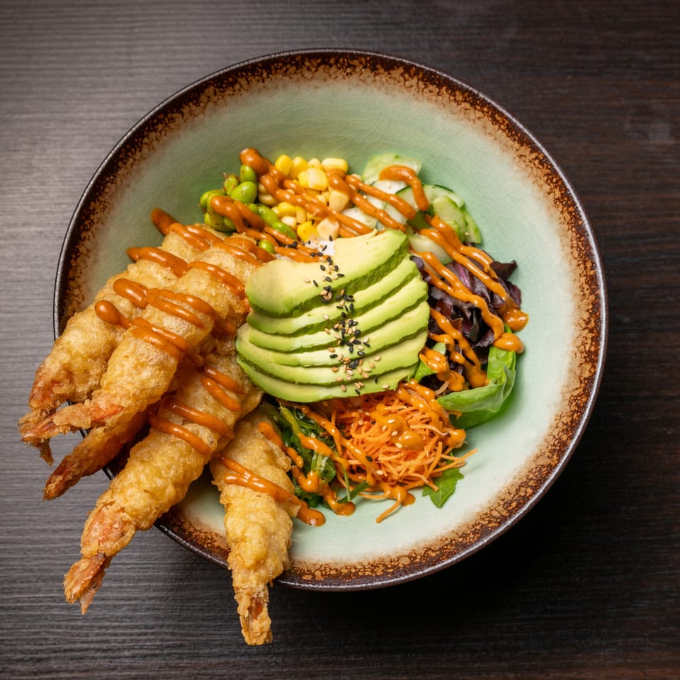 Tempura shrimp with avocado, corn, edamame, and greens, drizzled with orange sauce in a bowl.